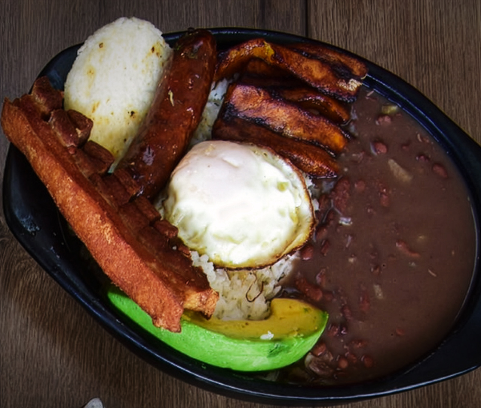 Cazuela de frijoles con chorizo, chicharrón, huevo frito, maduro, aguacate y arepa.